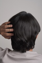 Fototapeta premium Rear view of young Asian man checking thick black hair and scalp health on white background