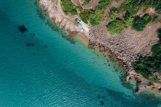Aerial summer landscape of a turquoise lagoon on Thassos Island, Greece, showing crystal clear water, beach, swimmers, paddleboards and rocky coastline.