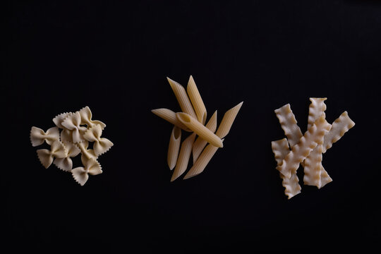 Different types of pasta: farfalle (butterflies), penne and ricciutelli on black background