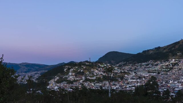 Panoramic view of Quito at dawn, with the iconic illuminated Virgen del Panecillo and the moon descending behind it.
