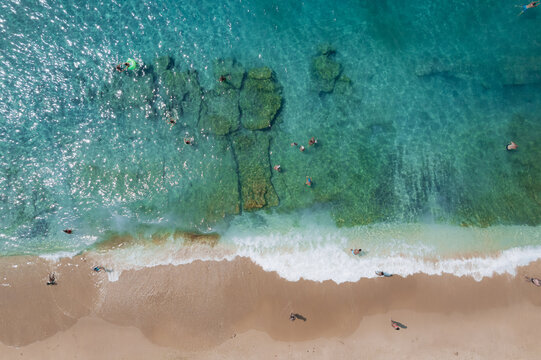 Aerial summer landscape of a turquoise lagoon on Thassos Island, Greece, showing crystal clear water, beach, swimmers, paddleboards and rocky coastline.