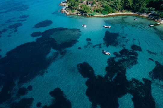 Aerial drone of a peaceful beach in Thassos, Greece, featuring transparent turquoise water, paddleboards, swimmers and a beautiful Mediterranean coastline.
