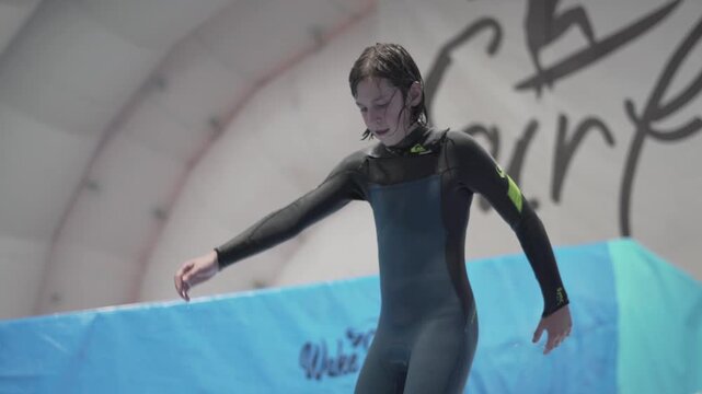Indoor surf sports club for children. Theme is active recreation and extreme sports on water. Student and coach on surfing training on wave simulator. Teenager surfing board at water park.