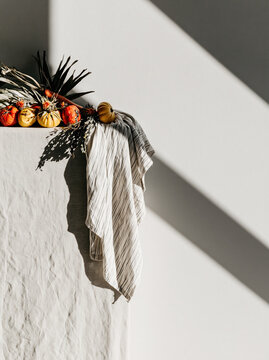 Autumn pumpkin decoration on white wall with striped cloth and strong shadow, rustic seasonal still life