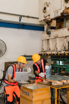 Technician measuring sheet metal bracket with calipers beside colleague holding laptop