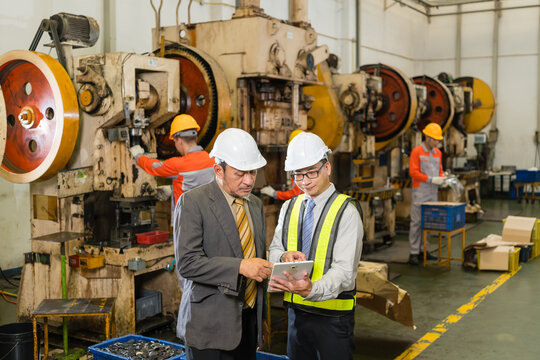 Plant manager and site engineer check inspection data on tablet near power press ensuring precision and quality in a modern industrial manufacturing environment with heavy machinery