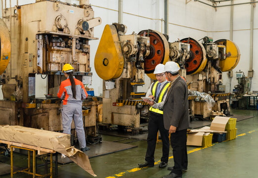 Engineer with tablet briefing senior manager beside female machine operator working at power press on factory floor