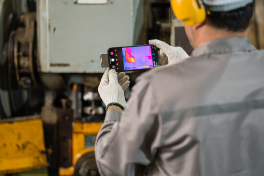 Power press machine operator scanning stamping die with thermal imaging camera supporting efficient production and workplace safety inside a busy metalworking factory setting
