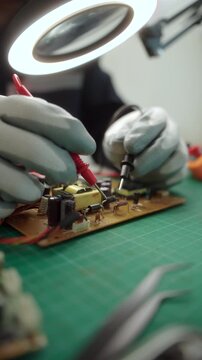 Close-up technician repairing a printed circuit board in a modern repair lab. PCB diagnostics, soldering electronic maintenance, right to repair. Sustainable technology and skilled technician.
