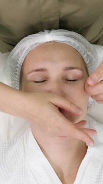 Top down view of a professional beautician performing a rejuvenating facial massage on a young woman lying on a couch, a relaxing skincare procedure for lifting and lymphatic drainage