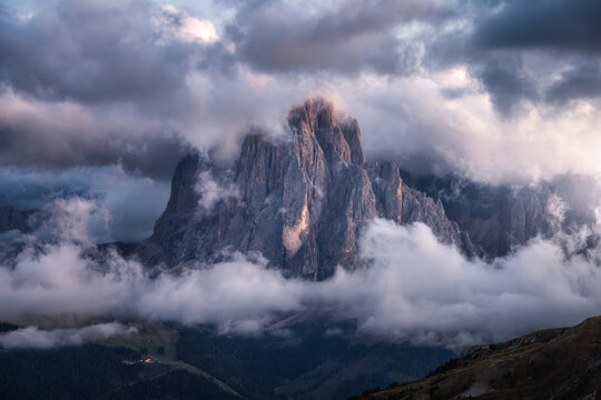 Dramatic mountain peak in clouds at sunset in Dolomites, Italy. High altitude rocky cliff top surrounded by fog in Italian Alps at dusk. Landscape with majestic mountain rock. Aerial view, top view