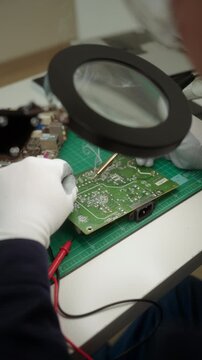 Close-up an electronics technician soldering a printed circuit board during electronic equipment repair. Precision engineering, PCB diagnostics, right to repair. Technology and electronics service.

