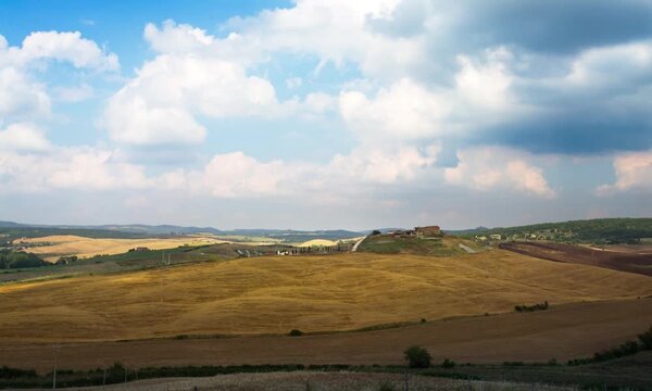 Time lapse of clouds moving over a golden harvested field and rolling hills on a summer day. Scenic Italy rural landscape footage for travel and agriculture projects