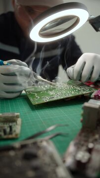 Electronics technician soldering a printed circuit board during electronic equipment repair. Precision engineering, PCB diagnostics, right to repair. Technology and electronics service.
