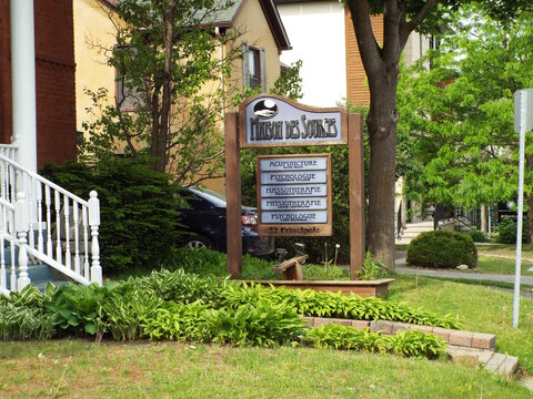 Gatineau, Quebec, Canada &ndash; June 7, 2026: A wooden "Maison des Sources" professional sign listing healthcare services stands outdoors along Rue Principale surrounded by lush greenery on Rue Principale.