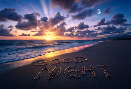 Good night text carved into sandy beach at twilight under moonlit sky with peaceful ocean waves washing shore during beautiful sunset cloud formation and golden horizon line.