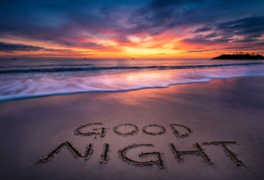 Good night text written in sand on beach during sunset with calm ocean waves rolling over shore and orange sky reflecting on wet surface creating peaceful relaxing evening mood scenery.
