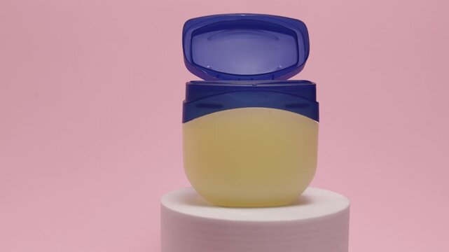 Petroleum jelly jar with blue lid on a pedestal against a pink background