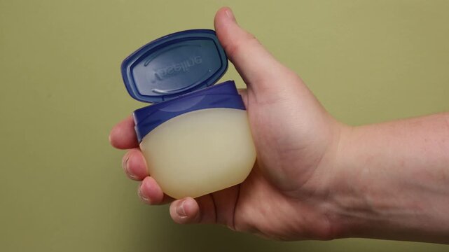 Hand holding petroleum jelly jar with blue lid open for application