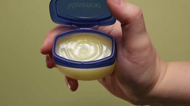 Hand holding open petroleum jelly jar for skin care and healing