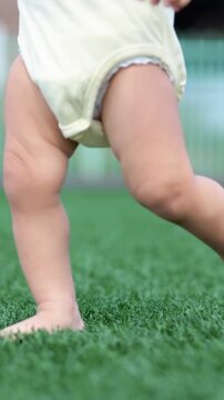 Adorable baby learning to walk barefoot on the fresh green grass, a close up of a toddler's legs taking the very first wobbly steps, symbolizing growth, new beginnings, and discovery
