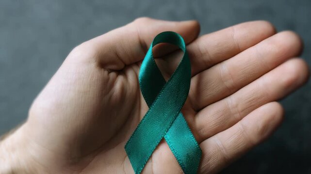 Teal awareness ribbon held in hand for medical support and health advocacy campaign, symbolizing mental health awareness and ovarian cancer support