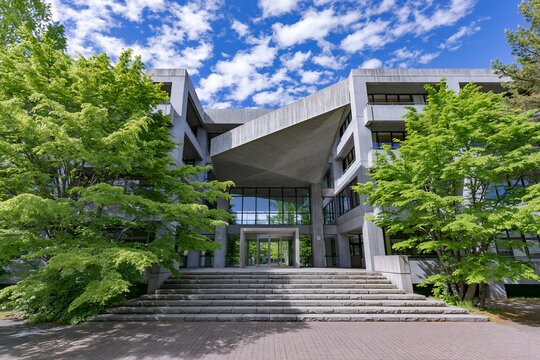 新緑と青空に映えるコンクリートのモダンな大学キャンパスの建物外観