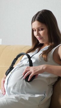 Expectant mother enjoying a peaceful moment, holding headphones to her pregnant belly, letting her baby listen to music, fostering a connection and stimulating auditory senses