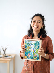Obraz premium Smiling young woman artist holding a painted canvas in her studio