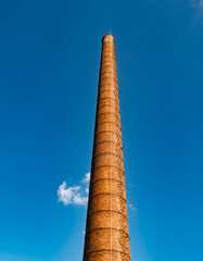 Fototapeta premium Tall Brick Industrial Chimney Against Clear Blue Sky