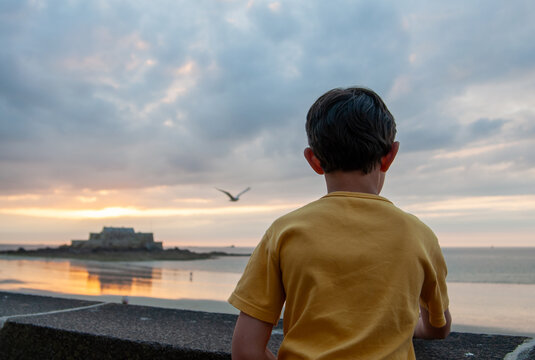 Au coucher du soleil, vu de dos, un jeune enfant au pull jaune contemple la mer &agrave; Saint-Malo