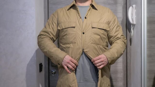  A man is fastening a jacket on his body it is a beige jacket with press studs. The jacket is being put on a man&rsquo;s body.