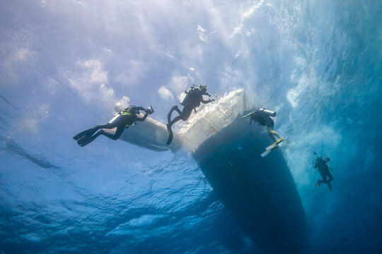 Group of scuba divers swimming under a safari boat hull in the ocean