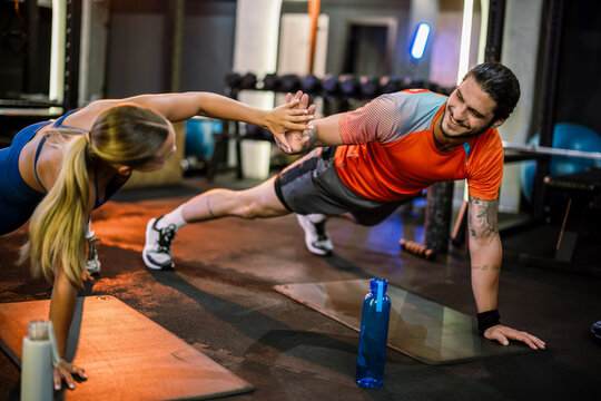 Athletic man and woman doing plank and high five in the gym