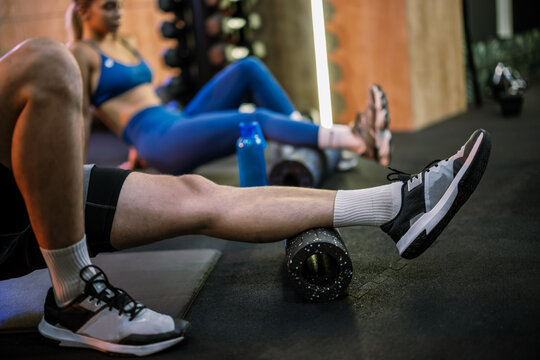 Fit couple stretching and relaxing their legs with foam rollers in gym
