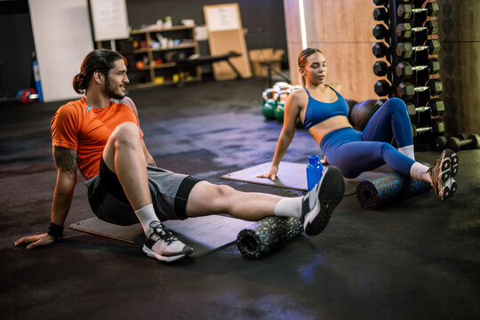 Athletic man and woman using foam rollers for muscle recovery in the gym