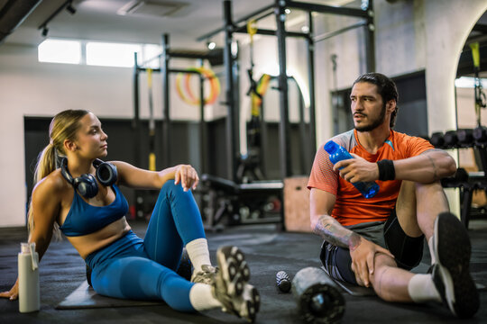 Athletic couple with protein shakes and headphones resting on gym floor