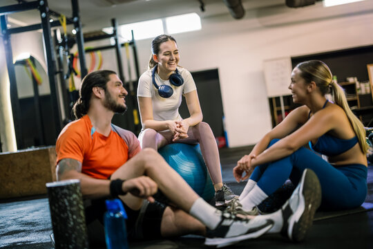 Athletic friends resting on gym floor and yoga ball with protein shakes