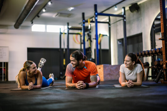 Three athletic friends resting and chatting on the floor in a modern gym