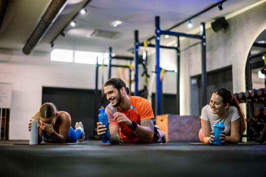 Three athletic friends resting with protein shaker bottles on the gym floor
