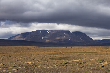 Fototapeta premium Barren volcanic mountain stands beneath heavy storm cloud in the Icelandic Highlands