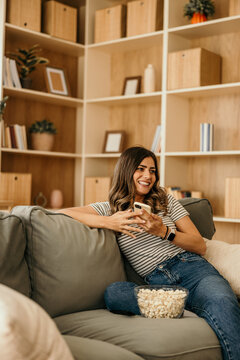 Woman relaxing at home, enjoying content on smartphone