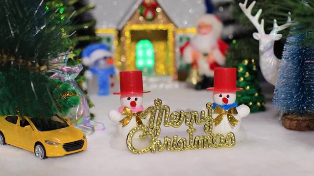 Between the fir tree branches with deer and a yellow car are two snowmen in red hats with letters
