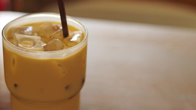Close up of a straw stirring refreshing iced coffee in a glass. Cold milk latte with ice cubes in natural light. Shot with selective focus. Morning cafe beverage and summer cooling drink concept.