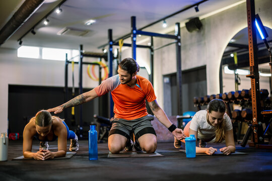 Personal trainer correcting form for two women doing plank in the gym