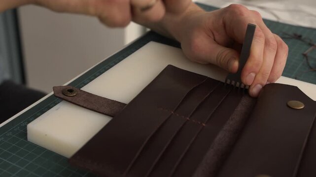 Craftsman punching holes in genuine leather wallet using hammer and stitching chisel in a workshop