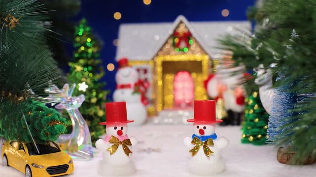 Between the Christmas tree branches are two snowmen in red hats with a yellow car against the backdrop of a Christmas house with a snowman and Santa Claus