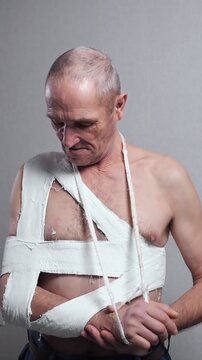 Worried mature man standing with a broken arm and shoulder in a plaster cast, showing the pain and discomfort from the injury while recovering from a serious accident on a grey background