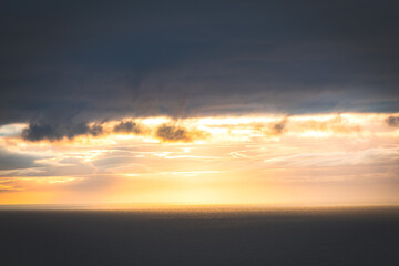 Fototapeta premium Golden sunset illuminates dramatic clouds above calm water in Iceland