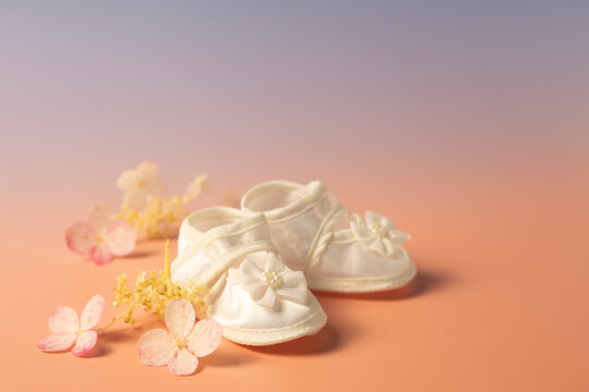 White baby shoes with pastel flowers on peach background, baby shower concept